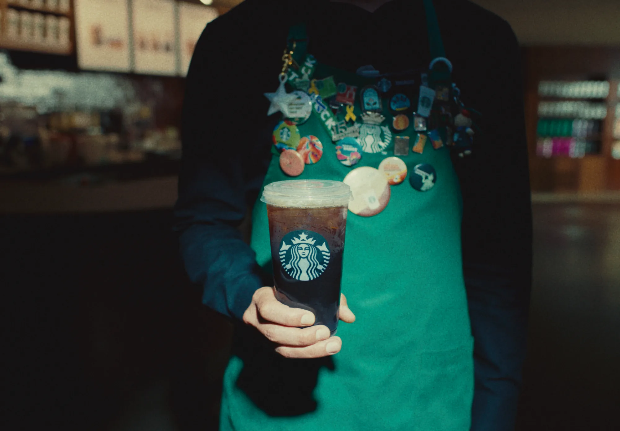 Copo Starbucks segurado à frente de um avental cheio de pins